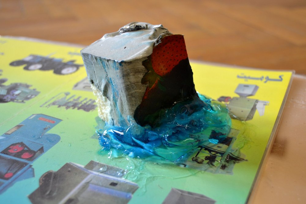  Paperweight #1, detail, 2015/16, Installation view,&nbsp;materials: Concrete with cardboard, aluminium foil and expanded foam, blue "Hair Code" gel, laminated company brochure (installation view),&nbsp;Roughly 6 x 6 x 6 cm. Photo: Nile Sunset Annex 