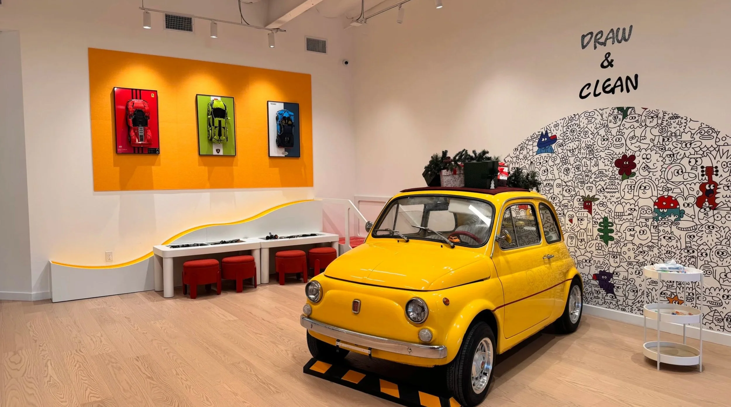 Yellow Fiat 500 interactive exhibit at Imagine Minds in Tustin, surrounded by custom artwork, LEGO play, and experiential interiors designed by A.Masow.