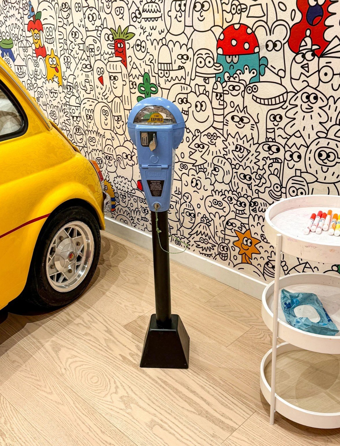 Yellow Fiat 500 and interactive play environment at Imagine Minds, featuring a retro parking meter, creative activity table, and custom illustrated wall.