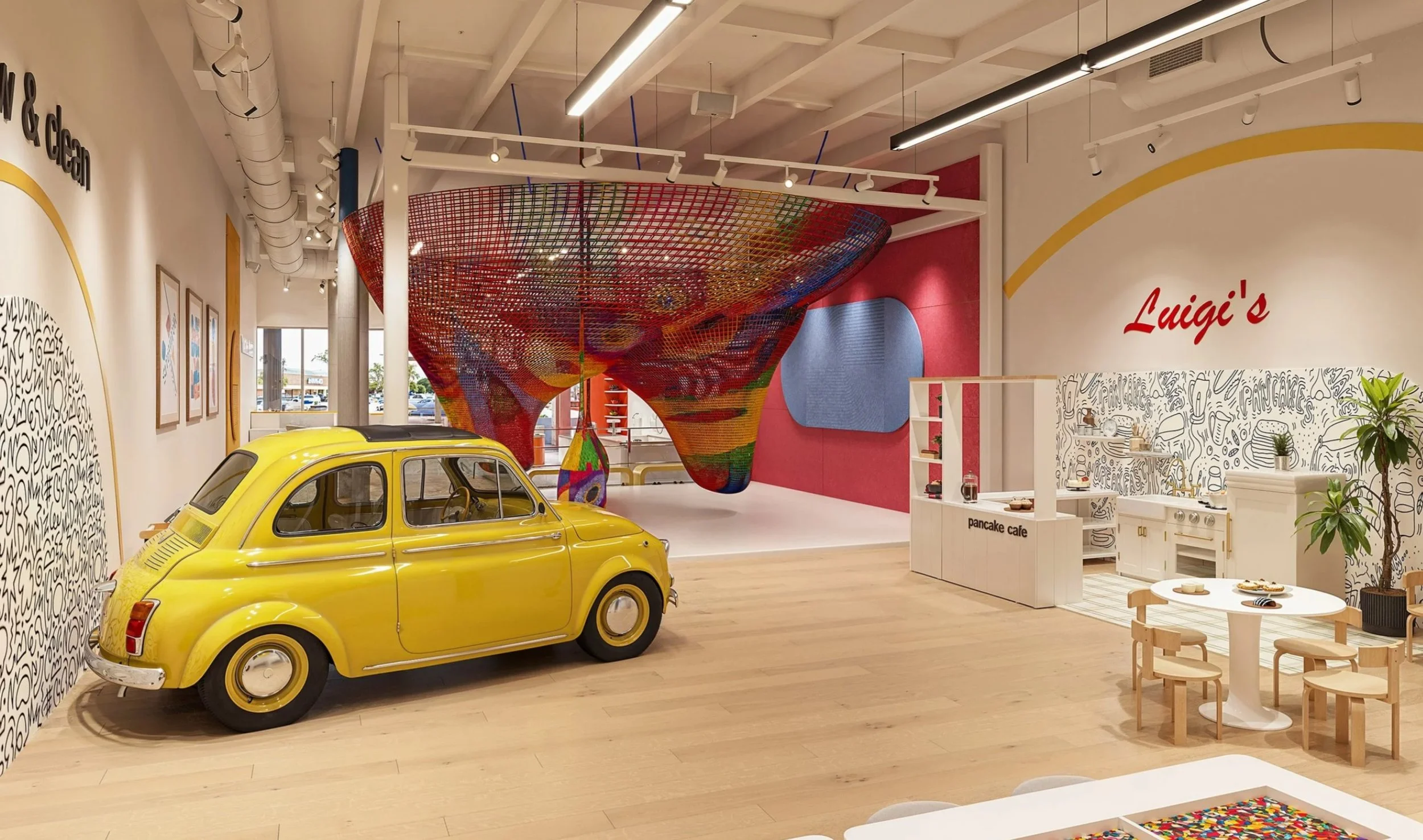 Interior of Imagine Minds experiential play center featuring a suspended rainbow climbing net, yellow Fiat 500, artwork, greenery, and custom interactive environments.