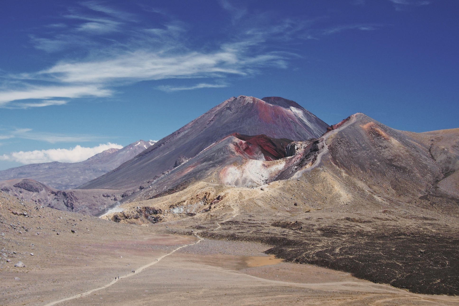 The large mountain in the back is Mount Ngauruhoe, the one in front of it with the deep red crater is where the Emerald Lakes are and that tiny little trail just shows you how massive it all is.