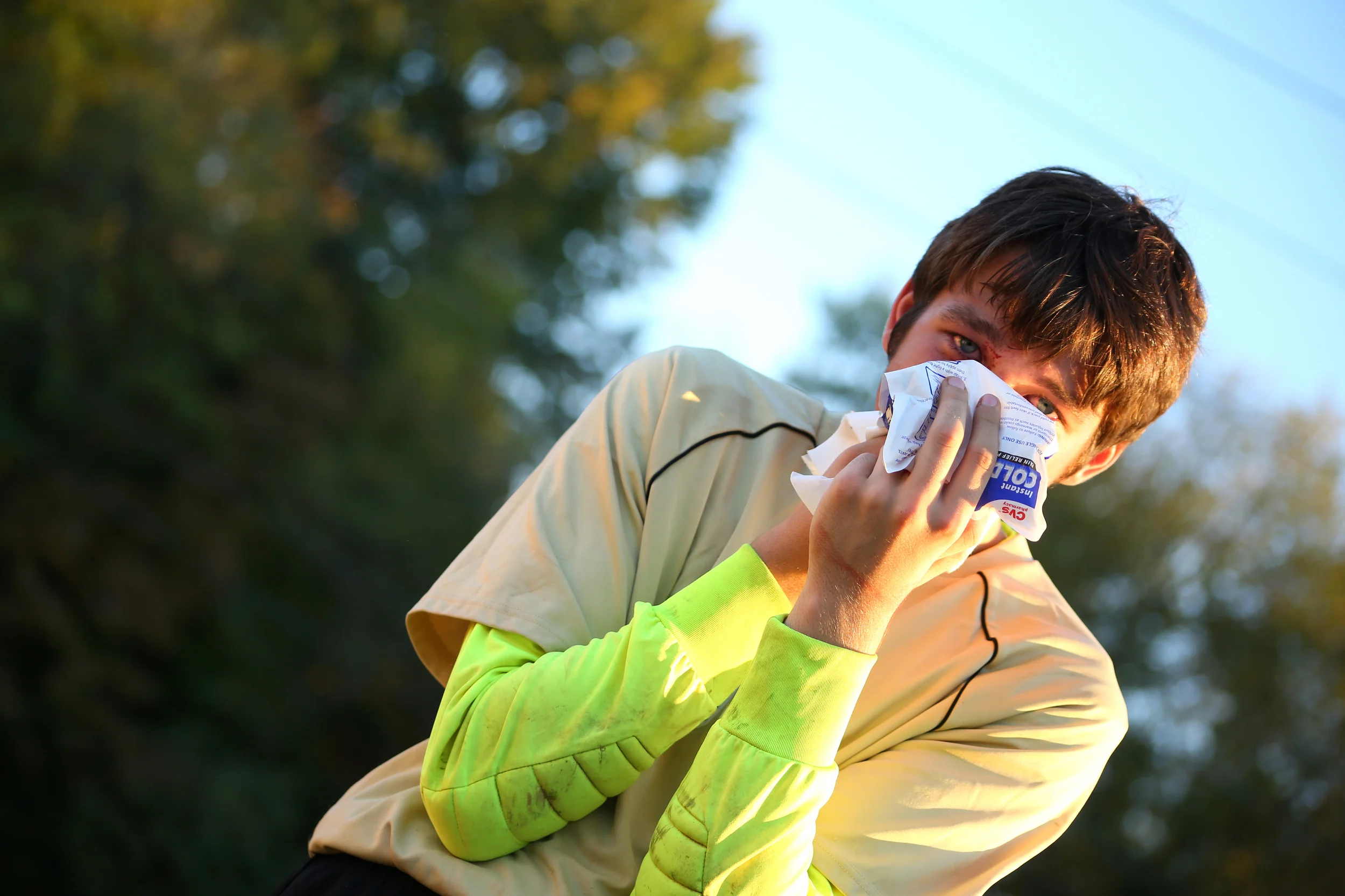 A boy clutches his nose at a soccer game after being kicked while saving a goal.