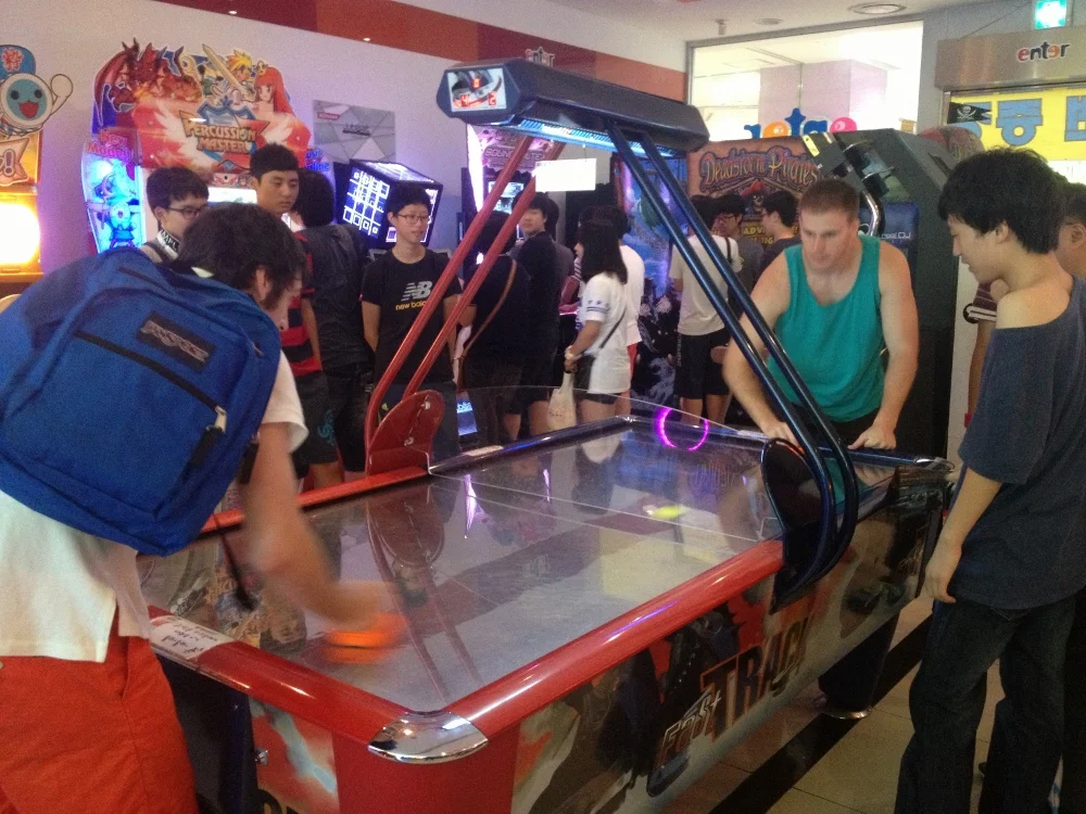 Jamie and Craig playing air hockey, with a small crowd of local kids watching on