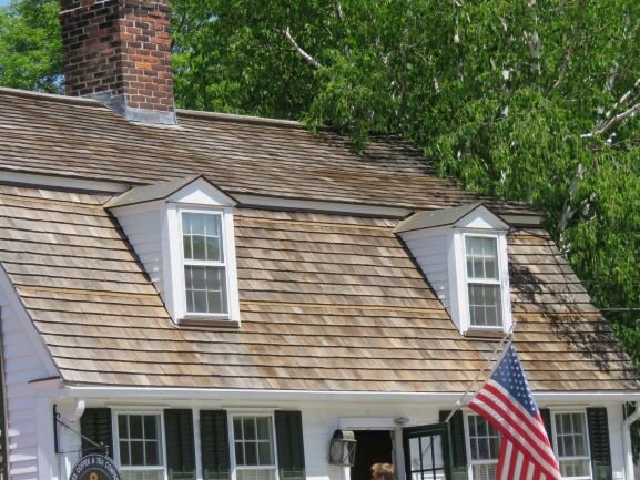 A cedar shingle roof like this one can last up to 40 years if it’s taken care of properly. Those tree branches are going to be a problem, as the shade keeps the shingles from drying out properly, which can result in rot and undesirable growths.