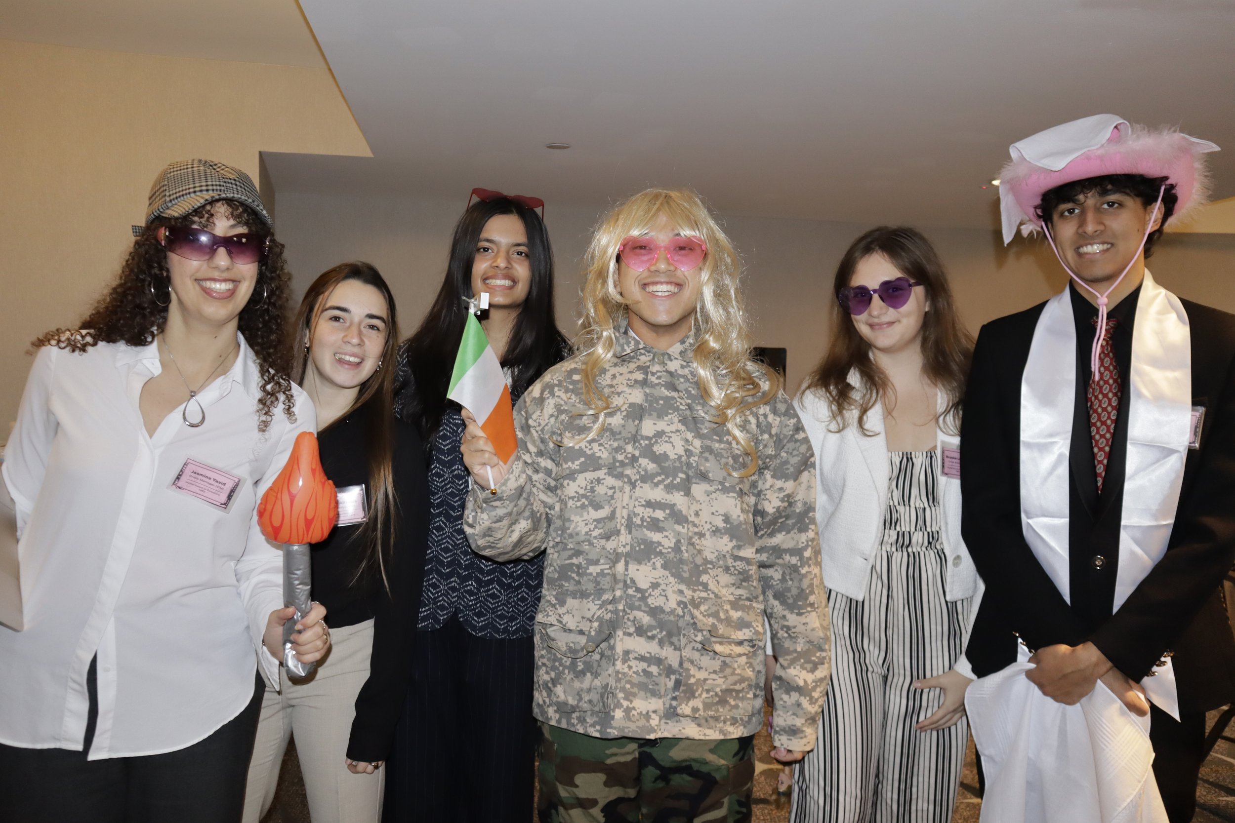 Group of six people dressed in costumes and accessories, smiling at the camera at a party or event.