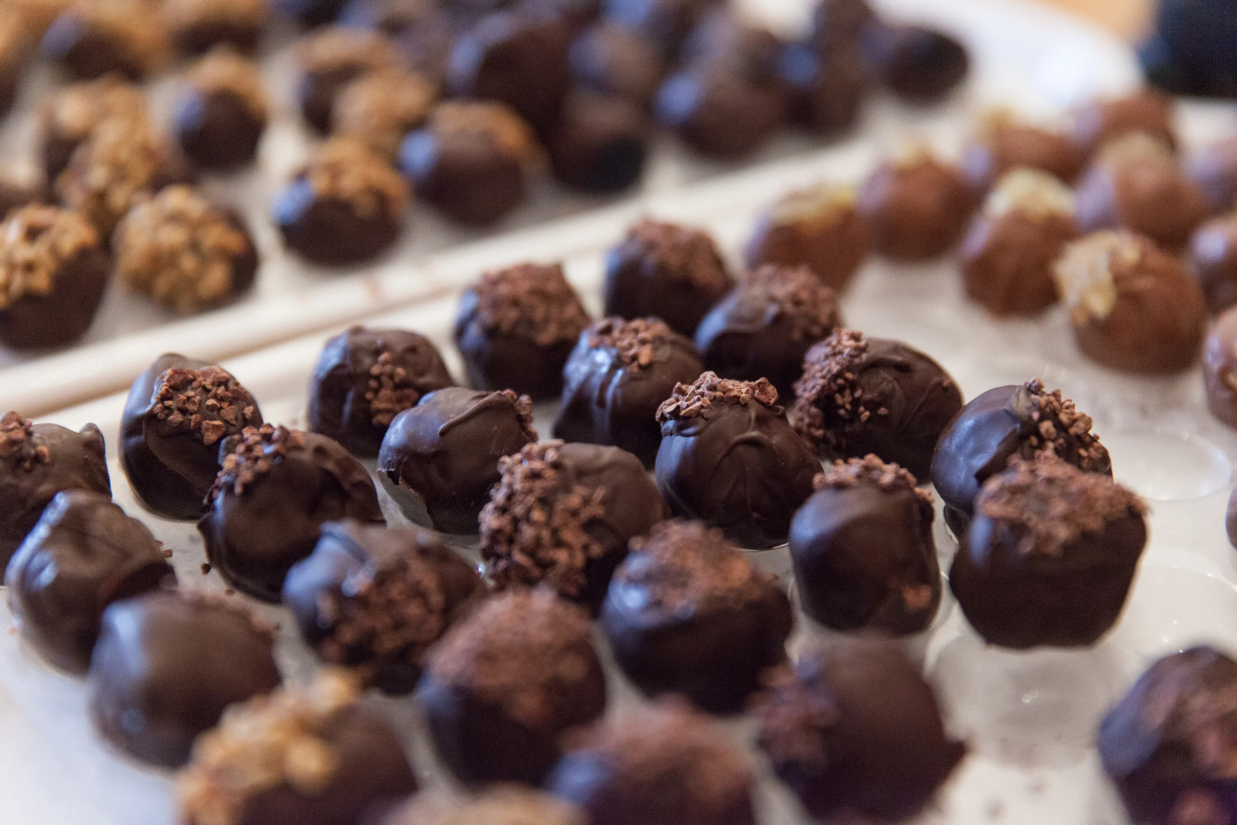 Close-up of chocolate truffles with some topped with crushed nuts, arranged on a tray.