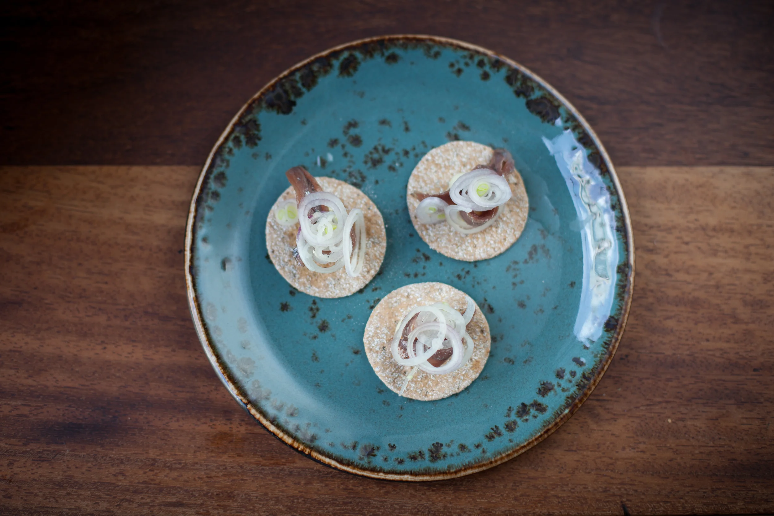 Three small round crackers topped with onion slices, served on a blue ceramic plate on a wooden table.