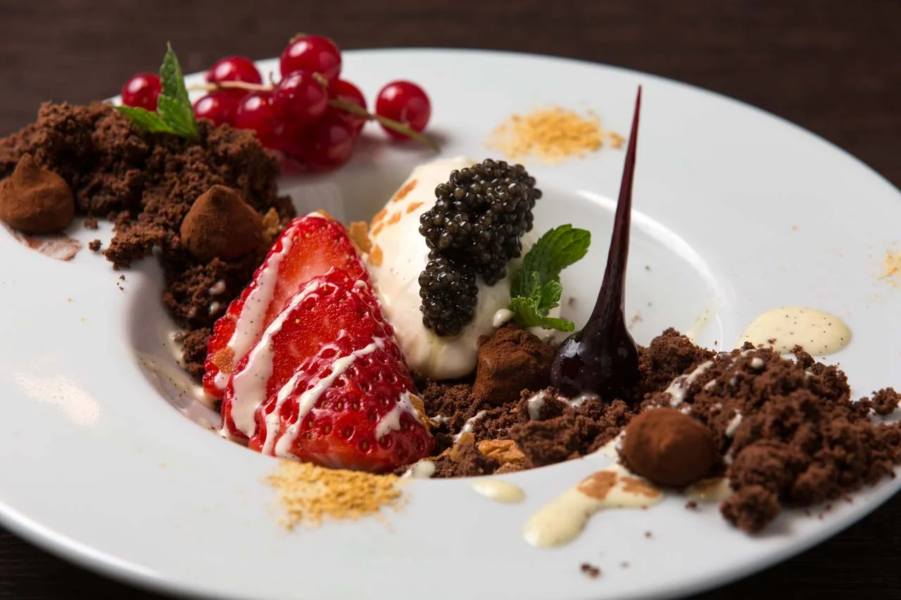 Dessert plate with strawberries, red currants, black caviar, mint leaf, chocolate crumbs, and various sauces.