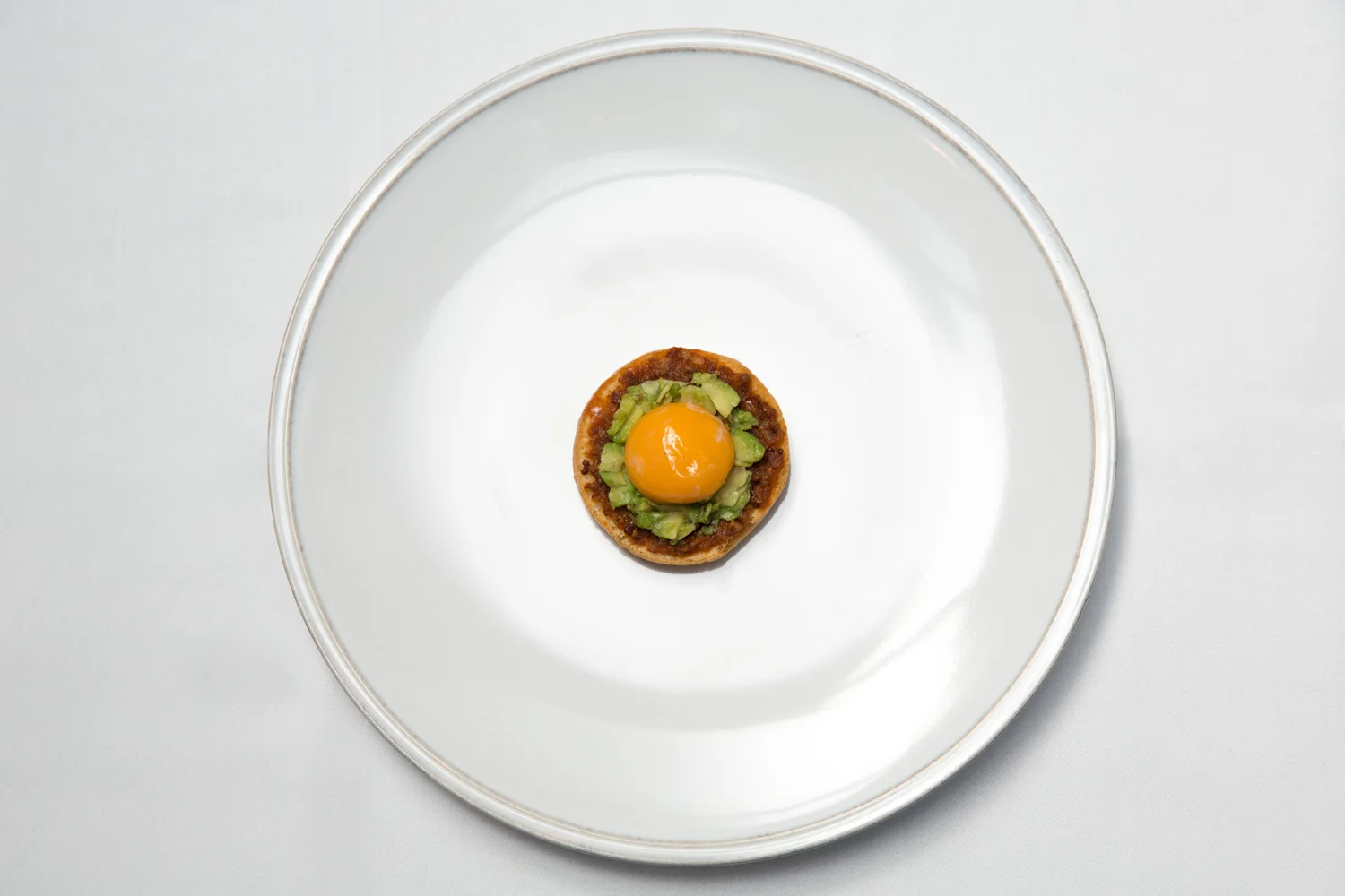 A small dish with a cooked egg yolk on top, surrounded by diced avocado and other ingredients, on a white plate.