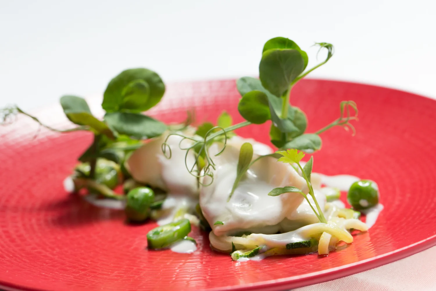 Poached eggs with microgreens, sliced green vegetables, and a white sauce on a red textured plate