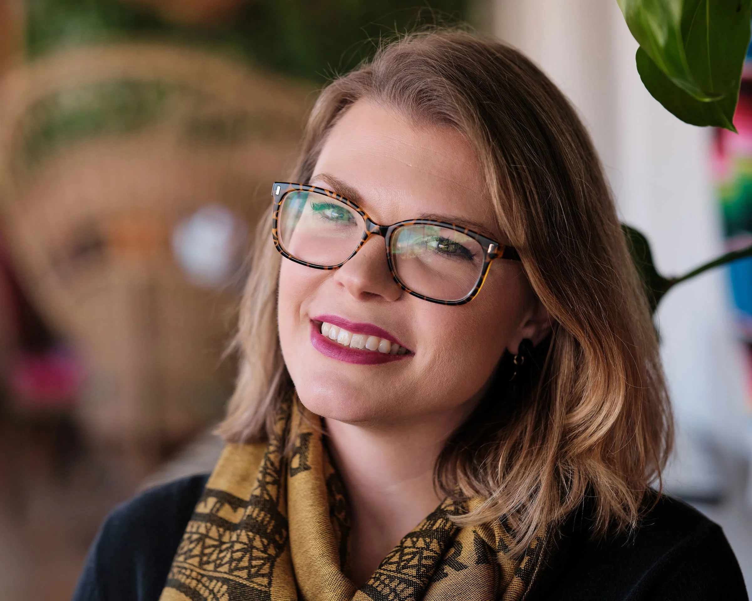 Close-up of a smiling woman with glasses, light brown hair, and a patterned scarf.