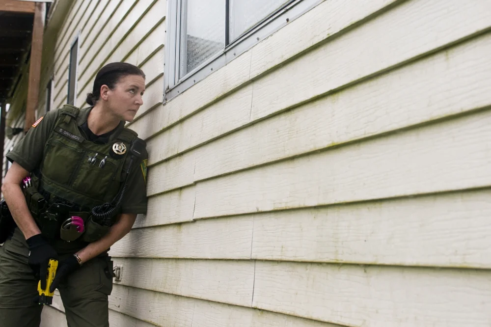  With her Taser in hand, Lewis County Sheriff's Deputy Sue Shannon peeks inside a window in the back of a house in Morton to see if anyone is moving around as Morton police officer Perry Royale works the front side of the house in an attempt to make 