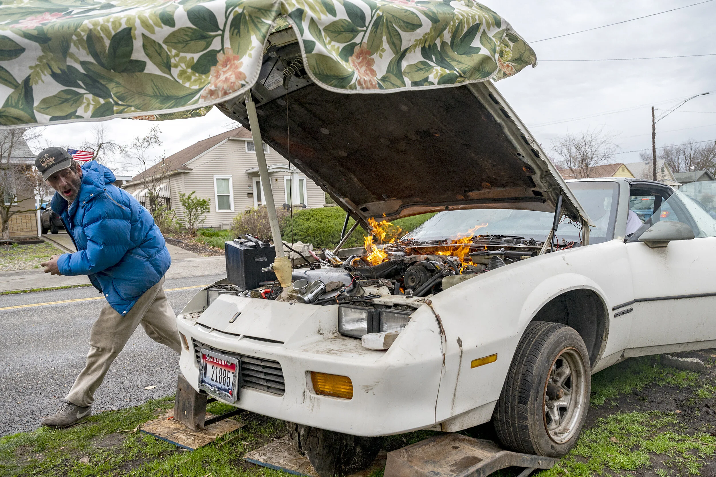  A porch umbrella being used as a rain cover couldn’t provide Rob Charpentier any protection as he runs away from the Chevy Camero that caught fire after he was spraying aerosol into the engine compartment while he and a some friends were working on 