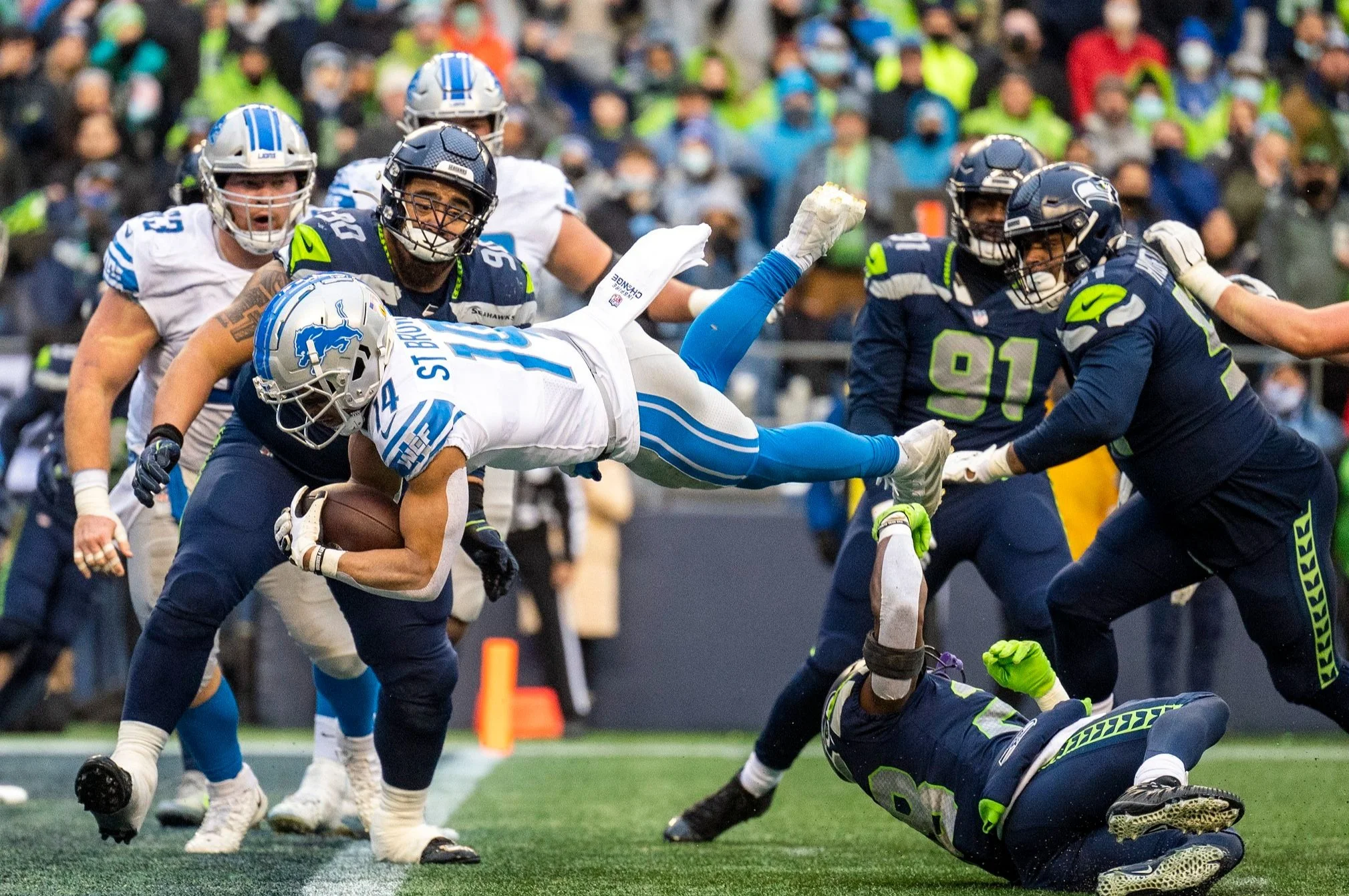  Detroit Lions wide receiver Amon-Ra St. Brown (14) dives  over a tackle attempt by Seattle Seahawks cornerback Ugo Amadi (28) for touchdown in the third quarter of an NFL game on Sunday, Jan. 2, 2022, at Lumen Field in Seattle. 