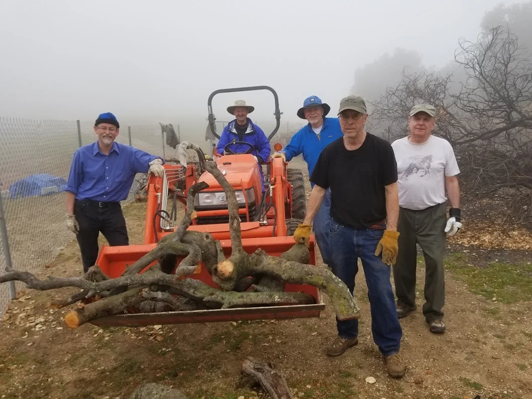 THE LOG TRANSPORT and storage team. (Left to right) Eric Turk, Sam Ervin, James Whedon, Bing Heckman and Jim Whitson. Not shown is Kyle Morrision who is at the storage area waiting to unload and stack this last bucket of logs. (Photo: Margaret Magnus, March 10, 2018)