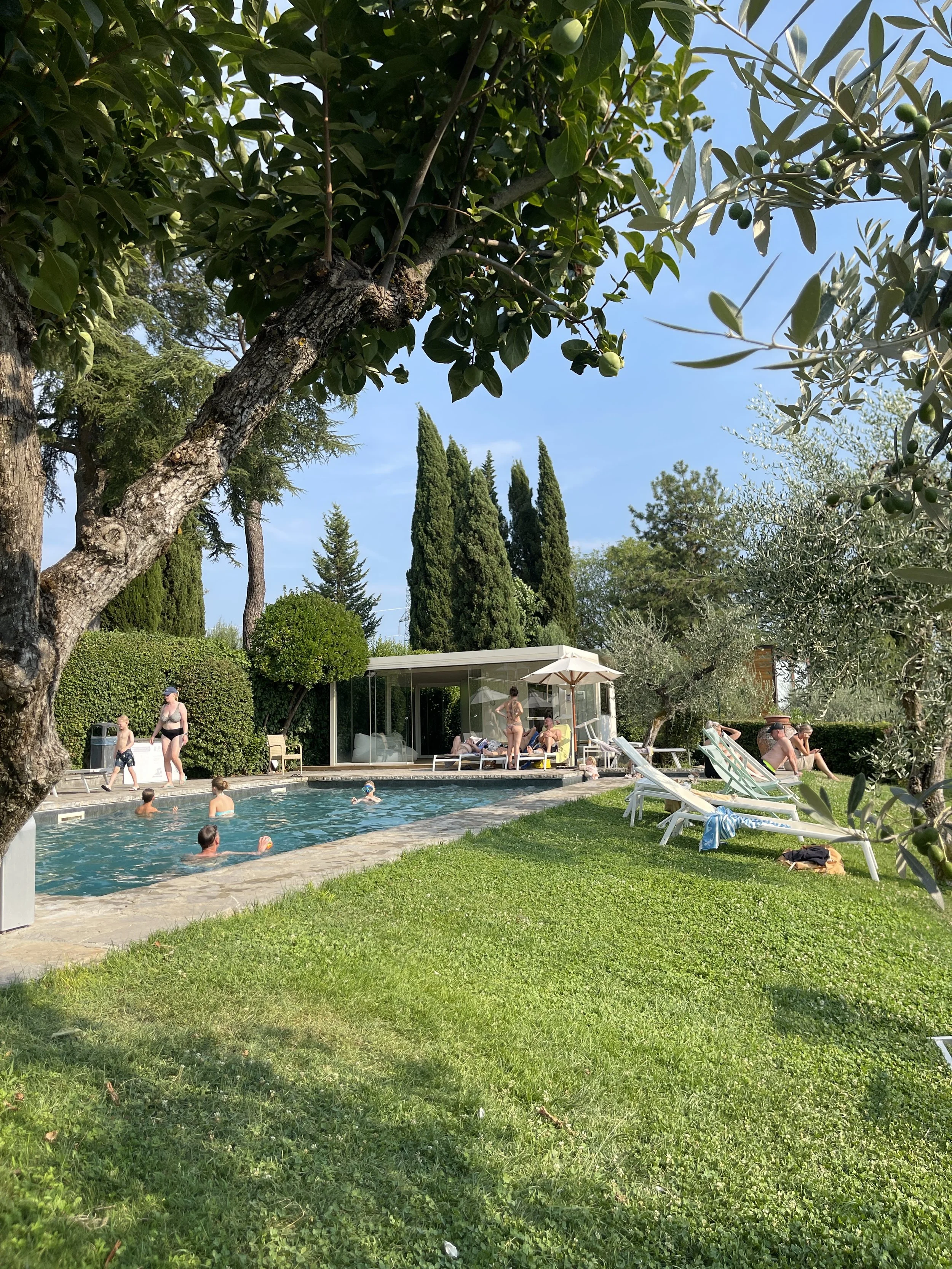 Gjester ved et hotellbasseng i Toscana med solsenger og parasoler i skyggen