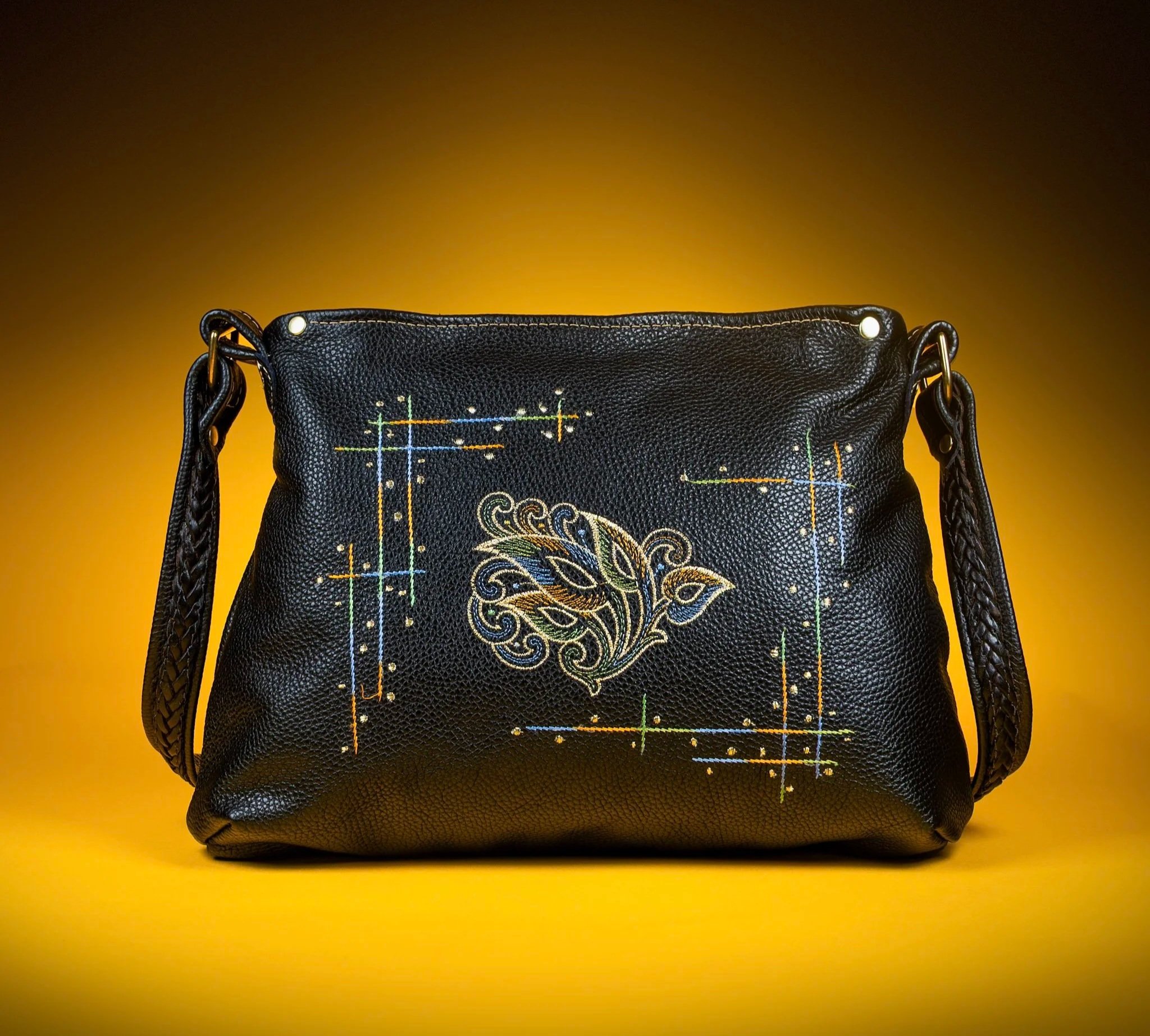 Black pebble leather handbag with colorful embroidery design, gold metal hardware, and braided strap. Peacock feather embroidery. Tradition meets modernity.