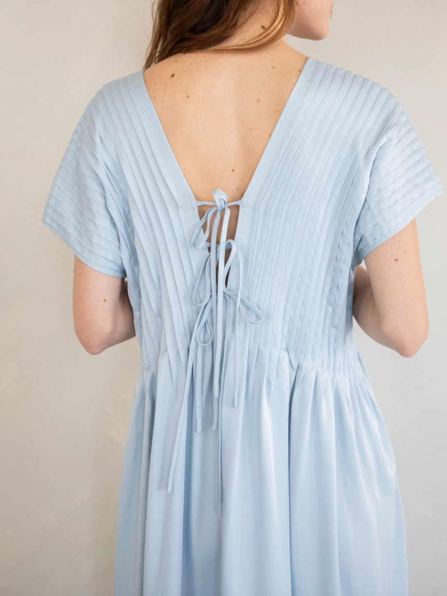 Back view of a woman wearing a light blue dress with pleated fabric on top and a lace-up back design.