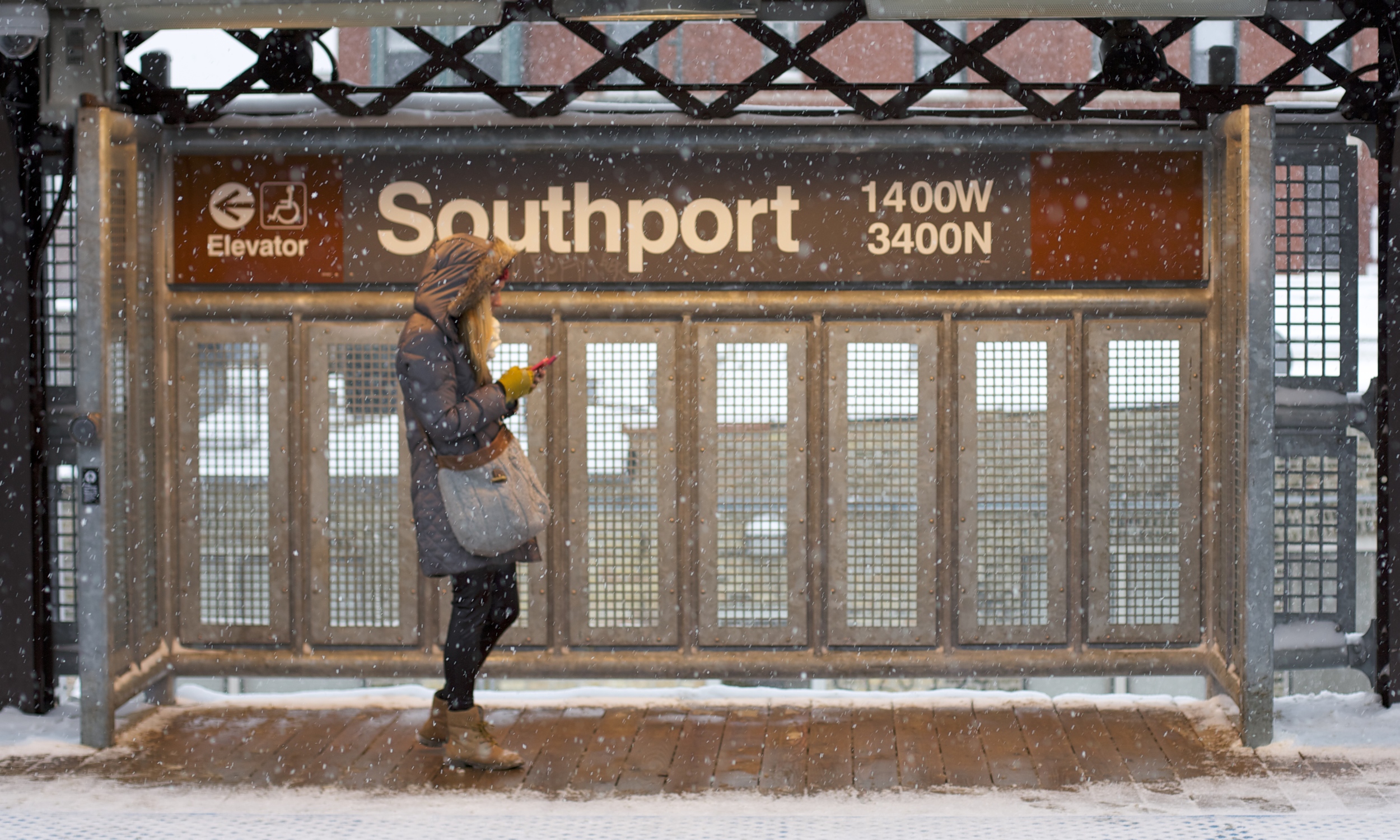 A woman check her phone in the Southport Station warming box as the snow falls