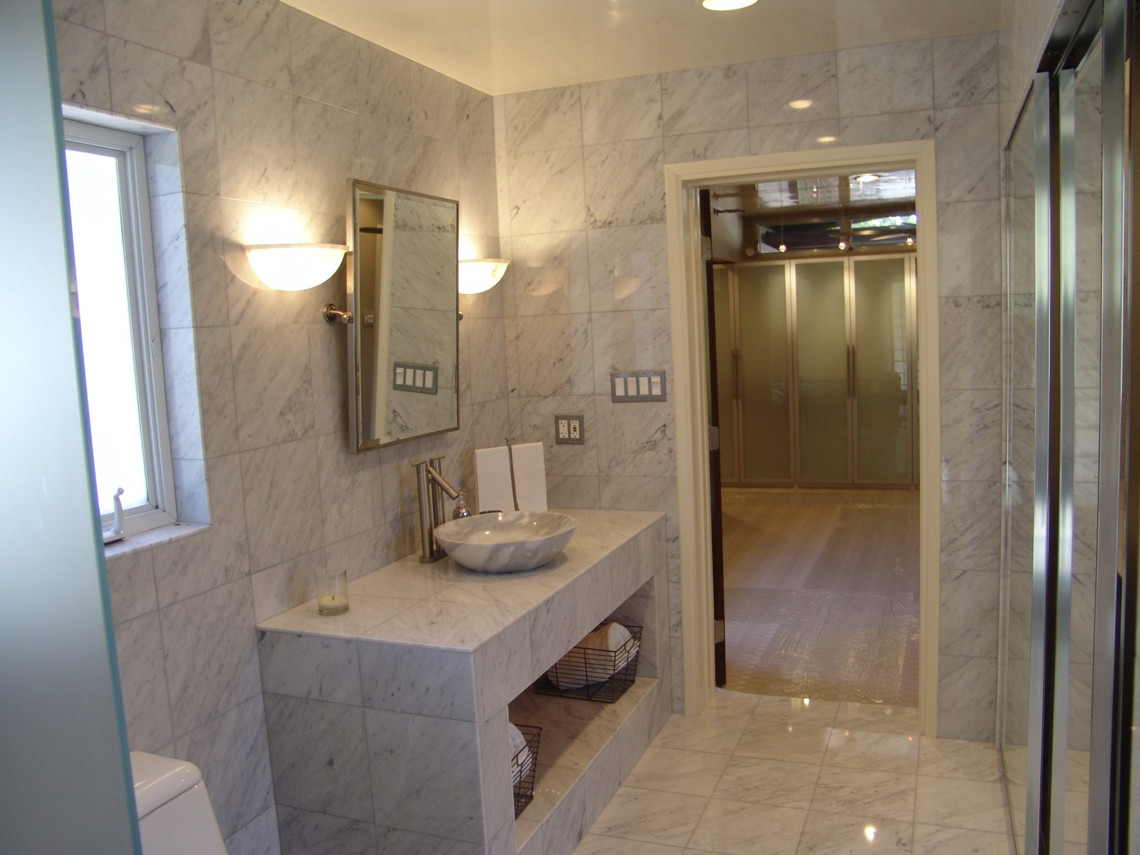 Floor-to-ceiling Carrera marble including a vessel sink for this master bath renovation with laundry and ample storage behind hidden mirrored doors.
