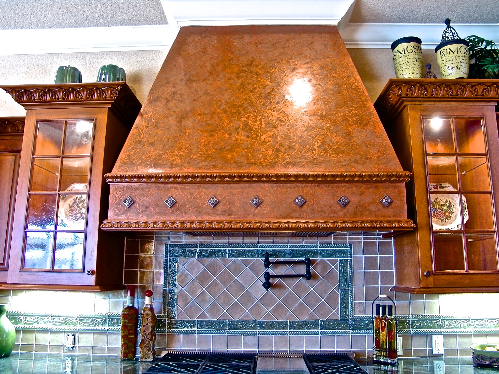 Drywall framed range hood finished in Venetian Plaster for a hammered copper look with bronzed applied ornaments for a faux stone finish.