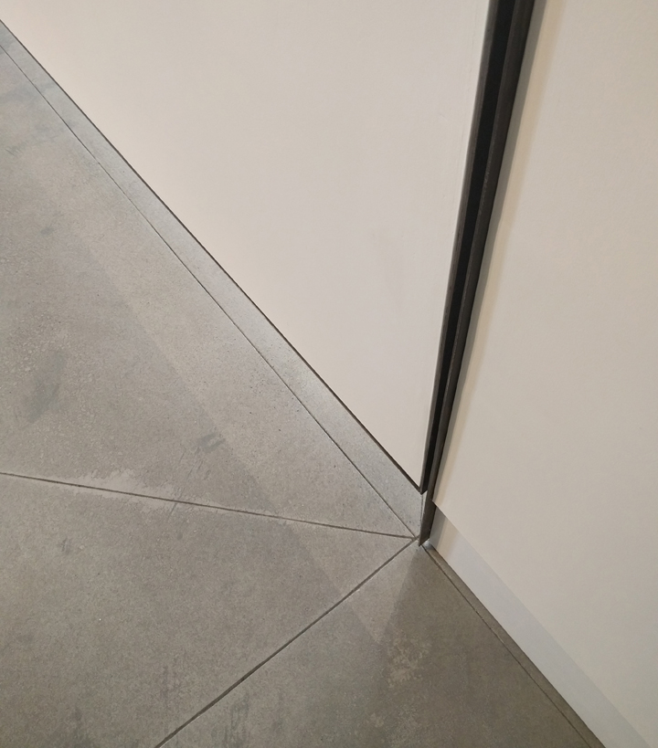 Convergence Detail where floor and walls meet. New concrete floor, with radiant heat below, marks the place where static wall and pivot wall connect. Blackened steel frame and hinge outlines this moment of connection.
