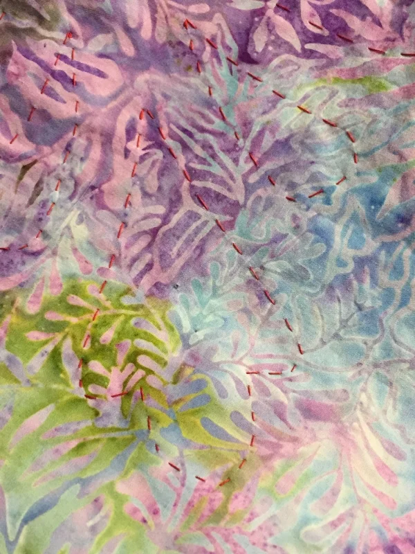 the design is basted through top and background with a thick thread in a color that contrasts the top fabric. Top view.