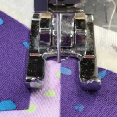 Left hand needle position of satin stitch goes into the background fabric right next to raw edge. I sight the left needle position and the raw edge as I satin stitch. Dark purple is my top fabric and is on the right of where I'm going to stitch. Light purple is my background fabric and is on the left of where I'm going to stitch.