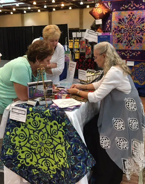 Margaret demonstrating her trace, baste, snip & stitch method for hand reverse appliqué at a quilt show.