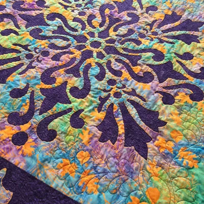 Illumination, Medallion X (56” x 56”) Machine reverse appliqued, long arm quilted with a small stipple in the interior reverse applique spaces and a feather motif in the corners of the medallion top fabric. Fabrics by Island Batiks.