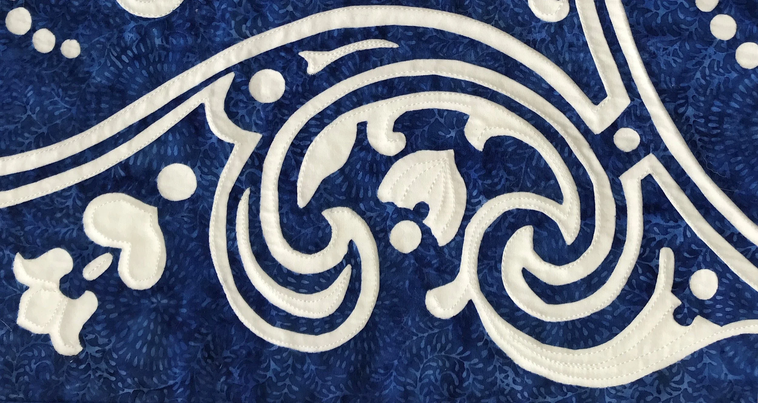 Close up of Eternal Spring, table runner VII (18” x 43”) hand reverse applique, machine quilted in the interior reverse applique spaces.