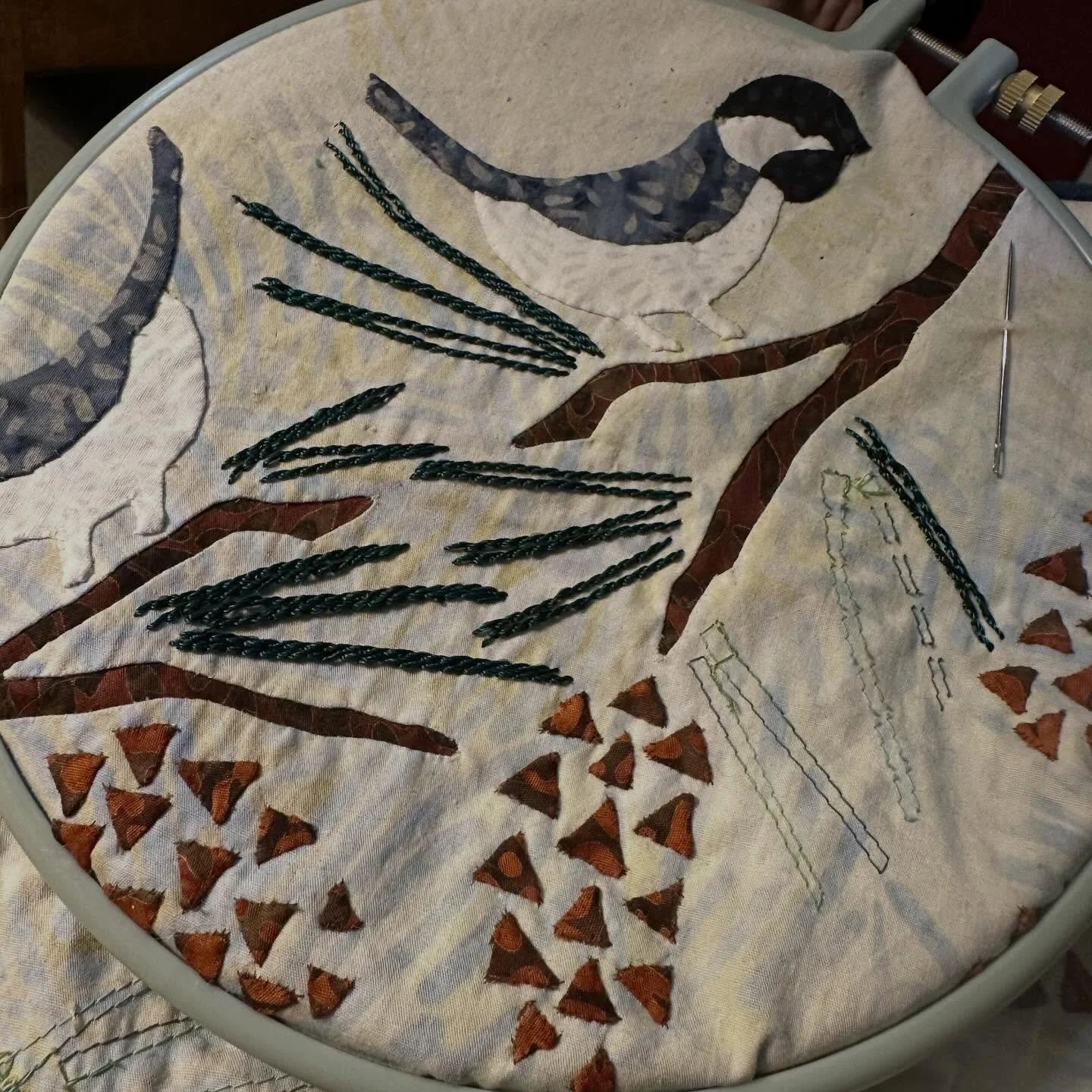 Chick-A-Dees are In my embroidery hoop, stitching on the pine needles with rayon thread.  Project for AQS SEAM Quilt Cruise-CANADA &amp; NEW ENGLAND, September 18-25, 2027 (class 1). Sign up at www.americanquilter.com/quilt-cruise/aqs-seam-2027-canad