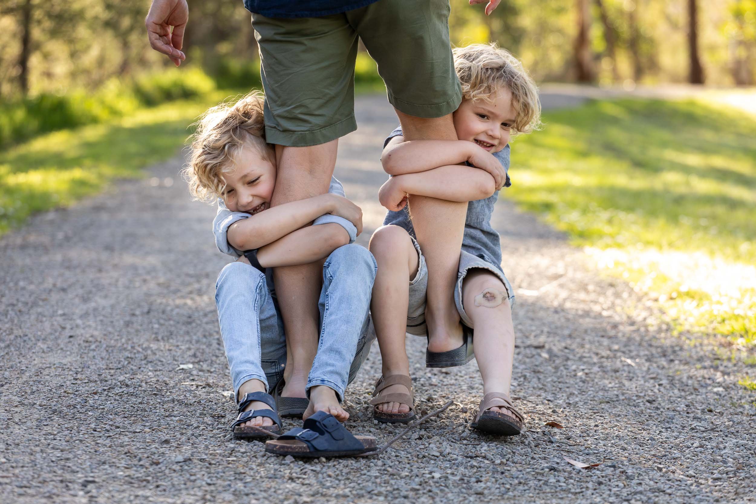  two boys hanging on dad’s legs in park in family photograph 