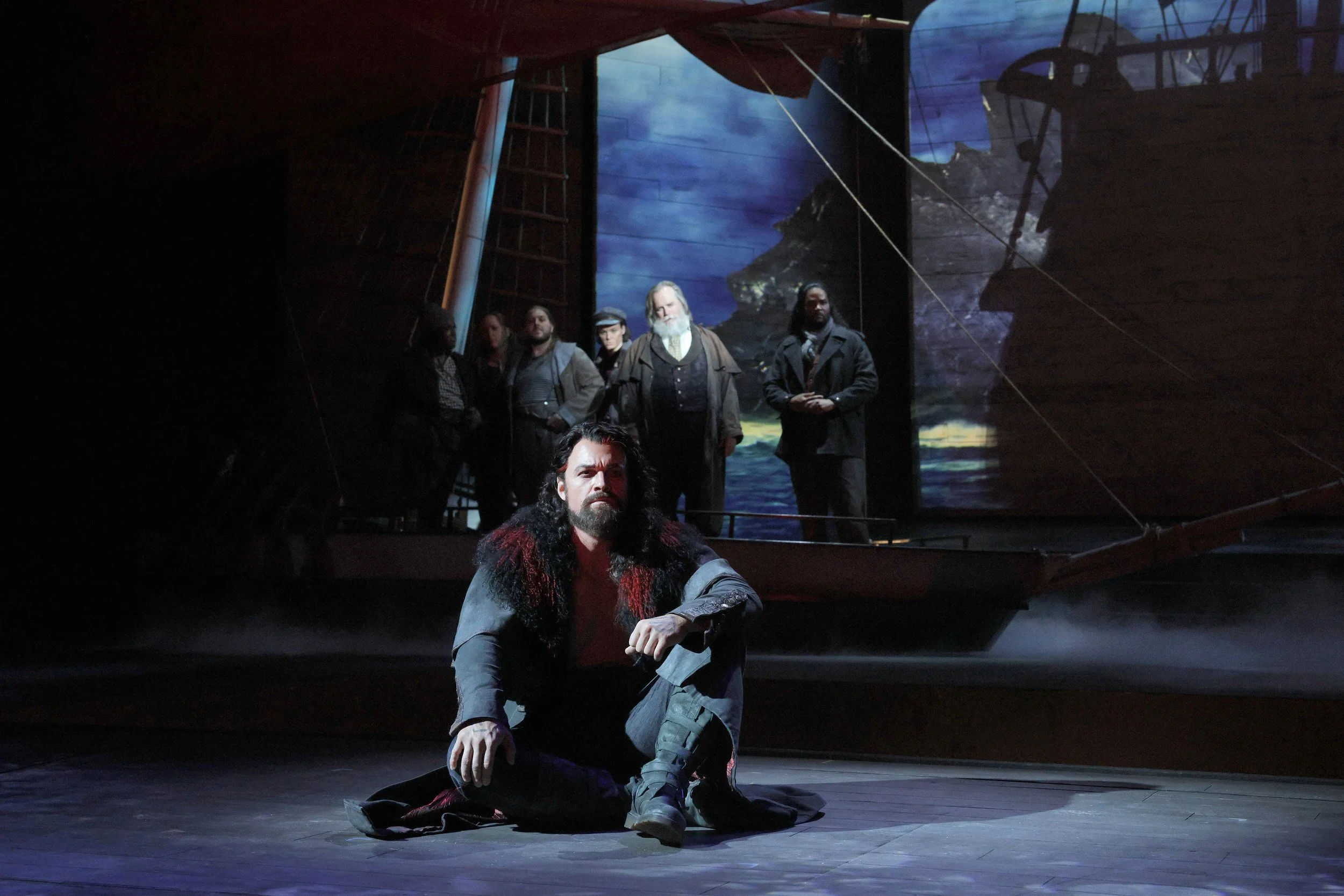 Ryan McKinny as the Flying Dutchman kneels while Kristopher Irmiter as Daland looks from behind during the opening duet of Richard Wagner's The Flying Dutchman.