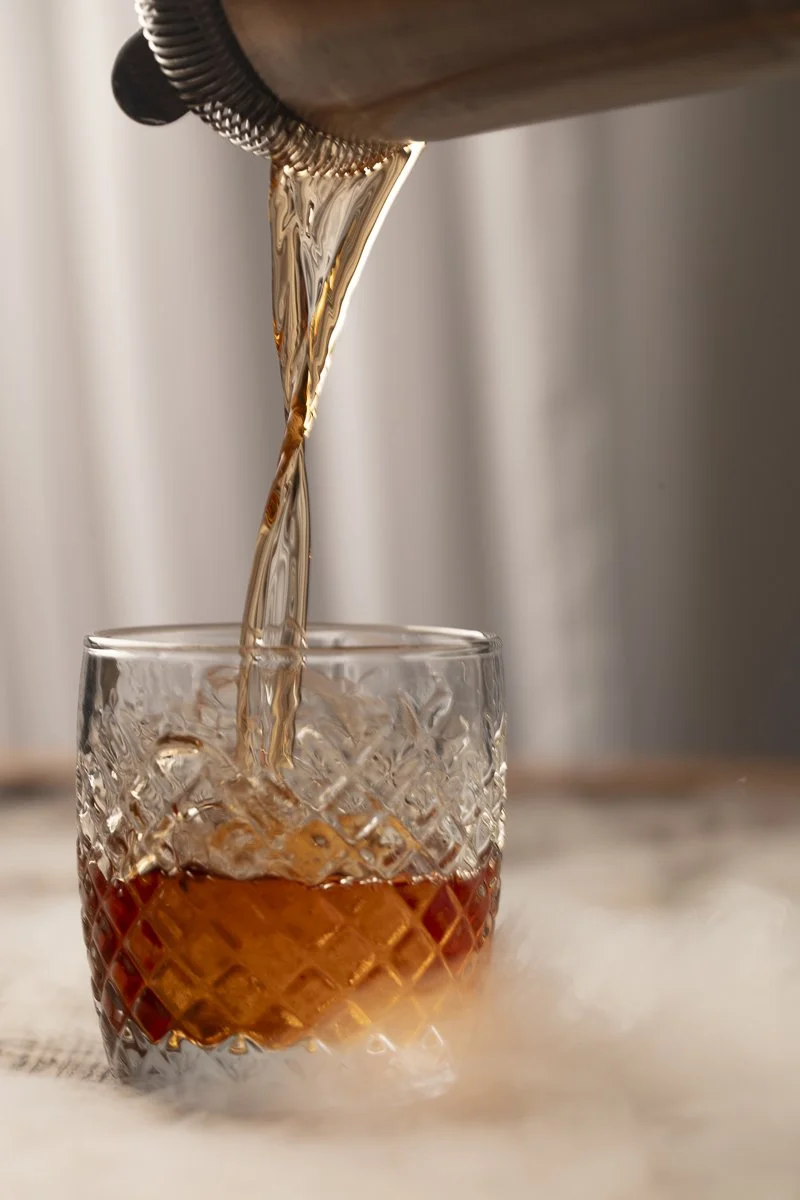 A close-up of a crystal glass with a diamond pattern, with whiskey being poured from a bottle into the glass. The whiskey appears amber in color.