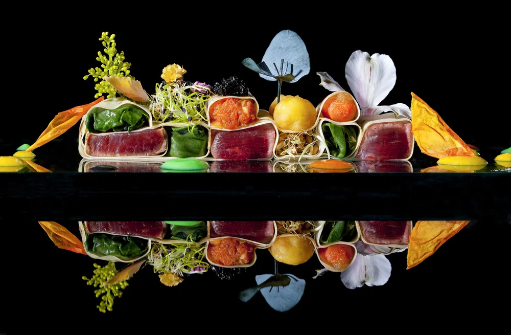 Gourmet dish with colorful ingredients, including microgreens, edible flowers, and thinly sliced meat, arrange