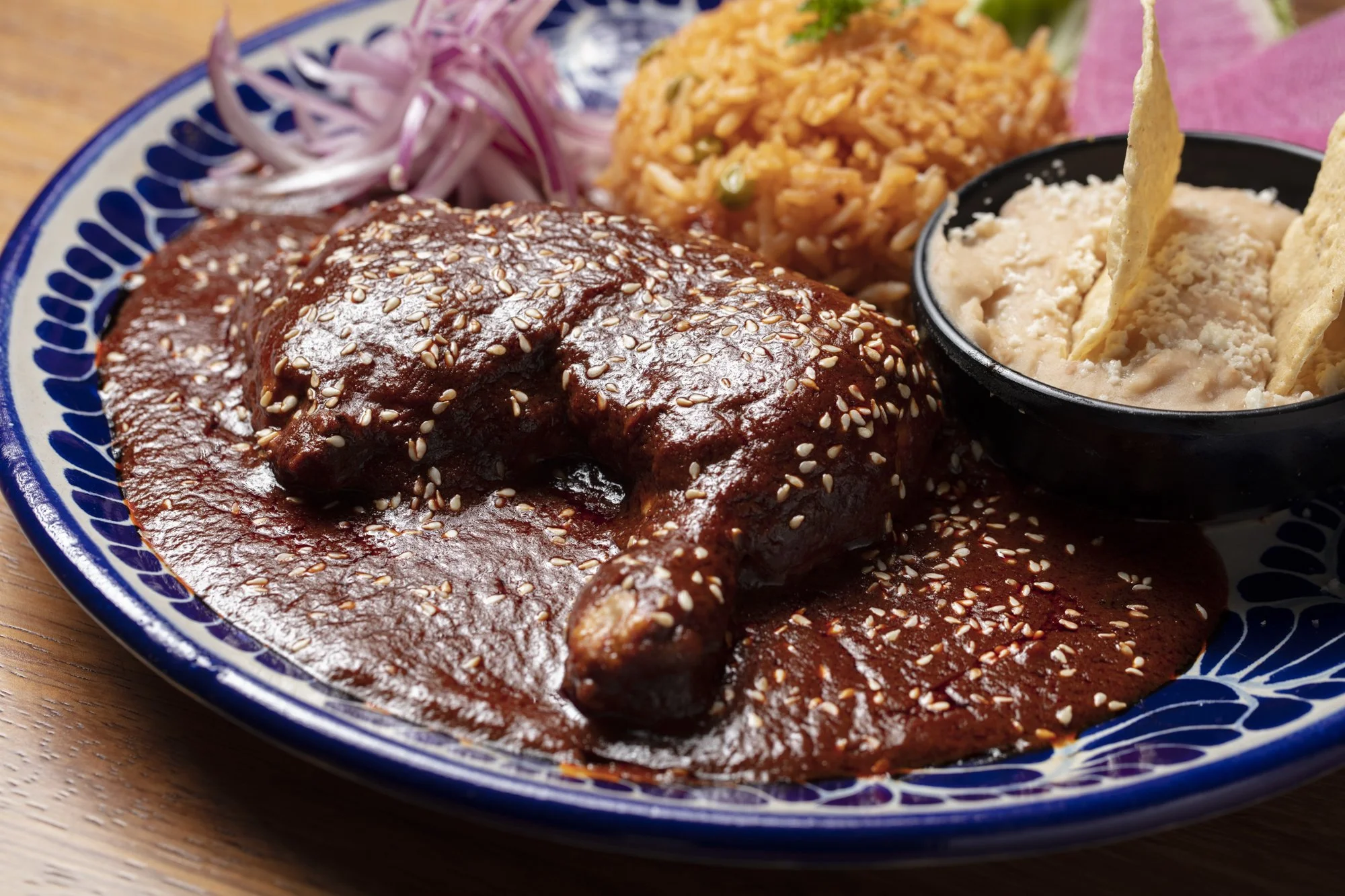 Plate with chicken in red sauce, rice, refried beans, and sliced onions with a pink napkin in the background. Los Angeles food photographer 