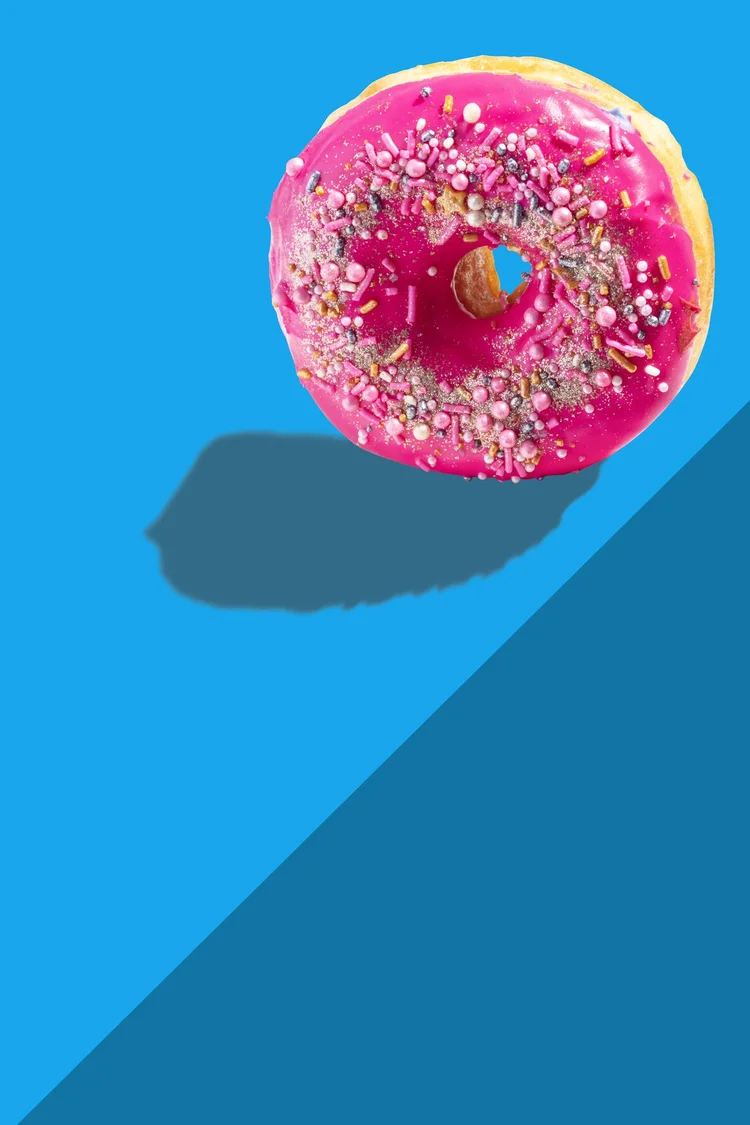 Pink frosted donut with sprinkles on a bright blue background - high key food photography