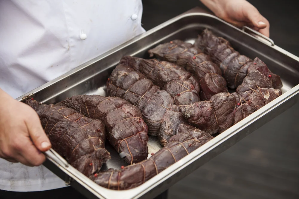 Chef hands holding a tray of seasoned meat, cookbook lifestyle photography