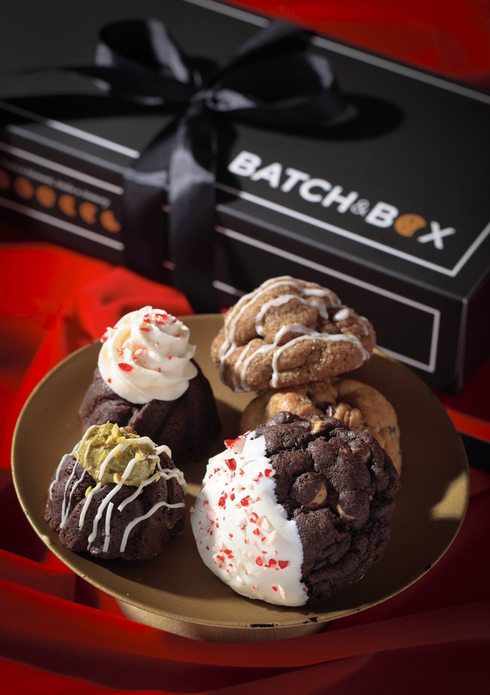 A gold plate with five decorated cookies and a black box with a white ribbon in the background. The box has th