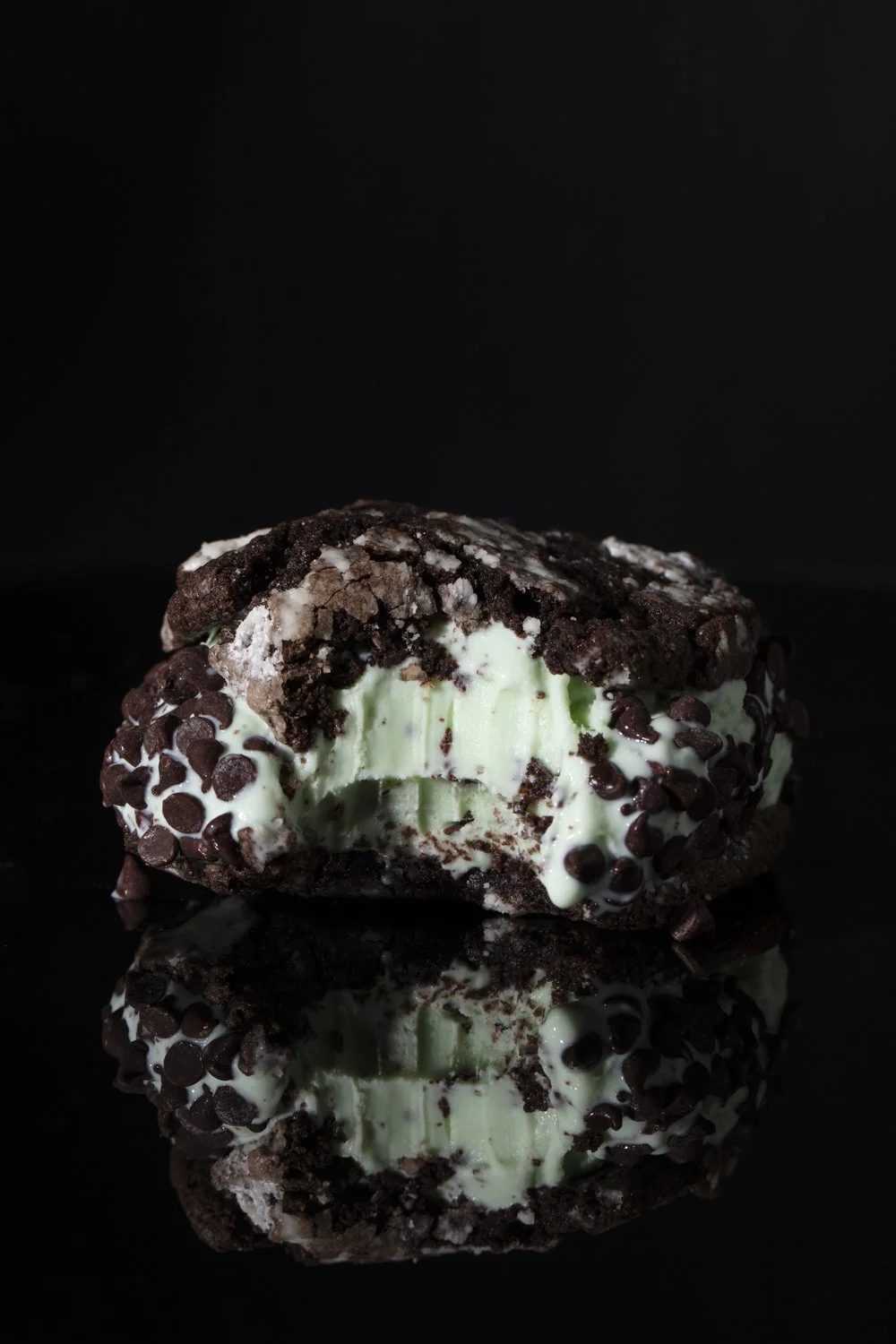 A close-up image of a chocolate chip ice cream sandwich with a bite taken out, showing vanilla ice cream and c