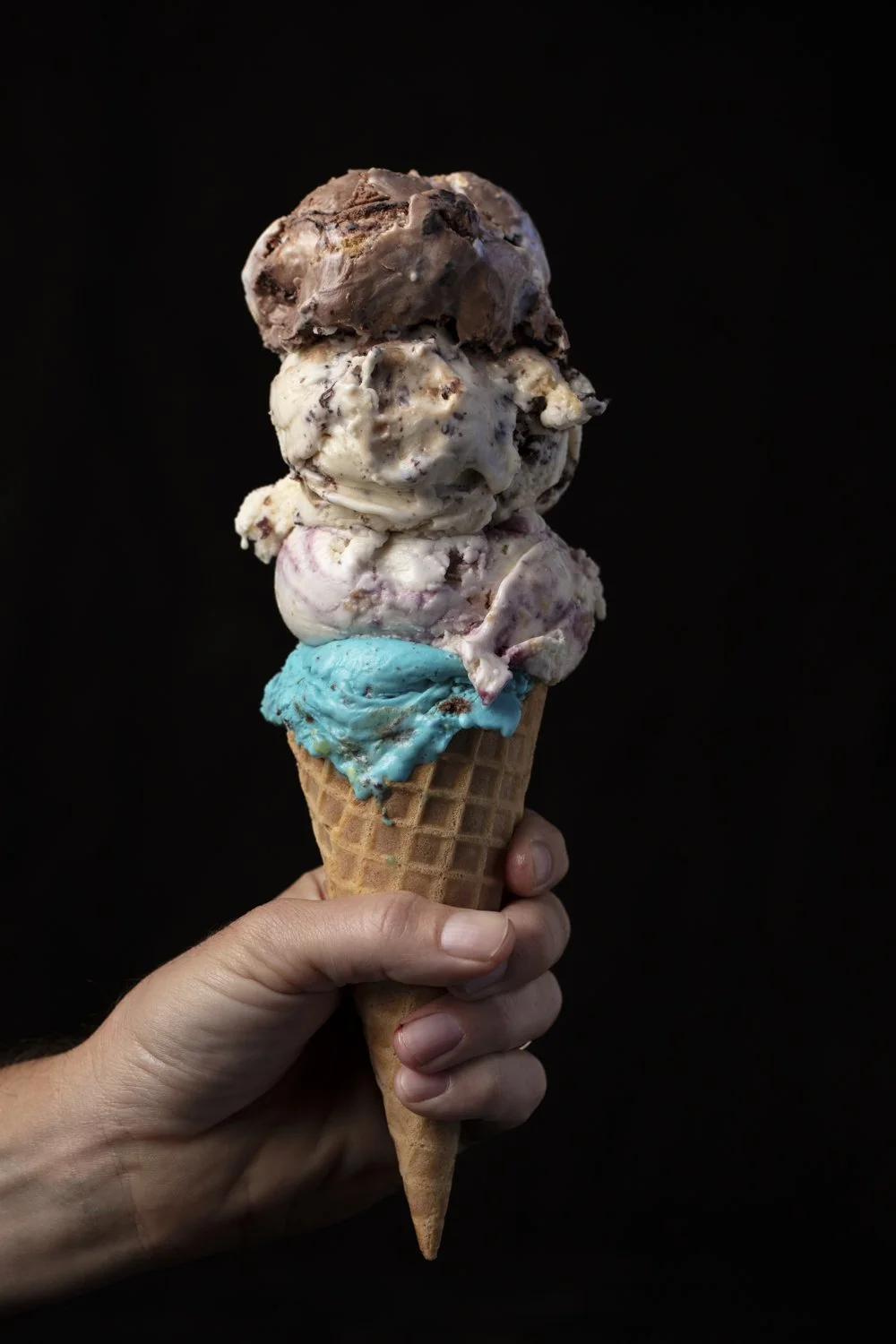 Hand holding a triple scoop ice cream cone against a black background