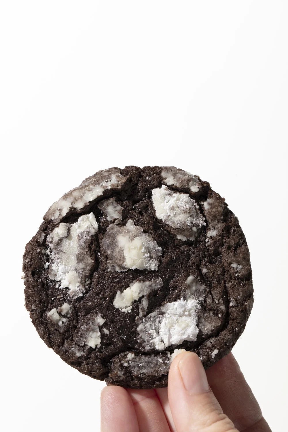 Person holding a large chocolate cookie with white chocolate chunks against a plain white background. Product and food photographer working in Los Angeles 