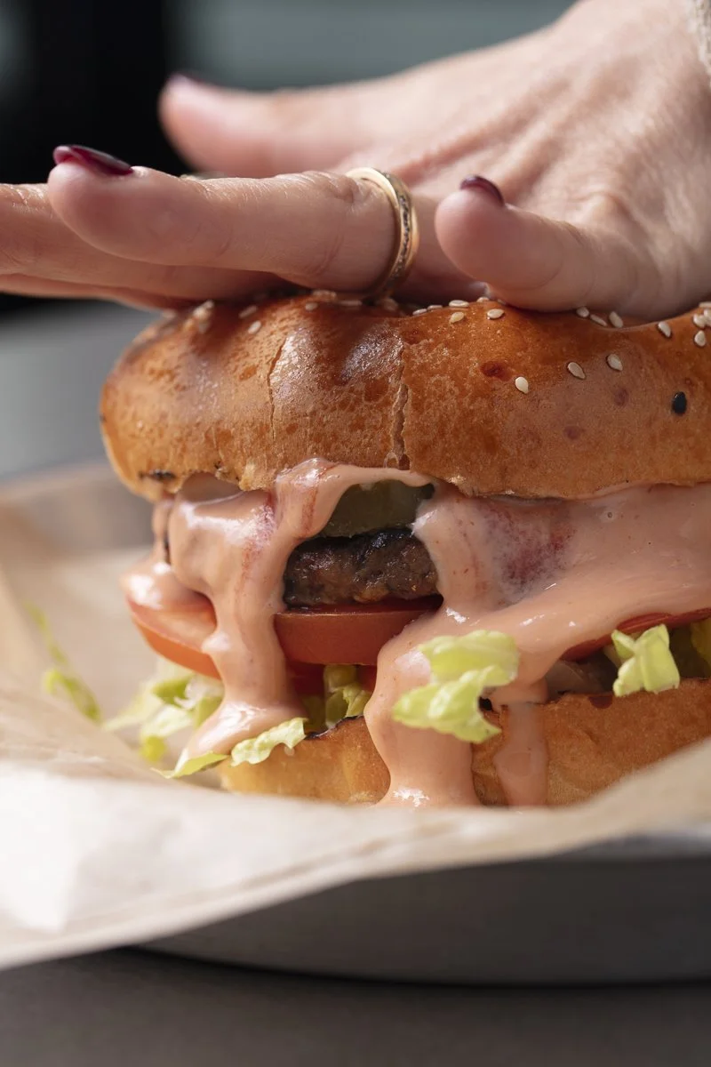Close-up of a cheeseburger with lettuce, tomato, melted cheese, a beef patty, and a sesame seed bun
