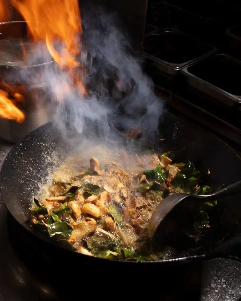 Stir-frying chicken and green vegetables in a wok with flames and smoke.