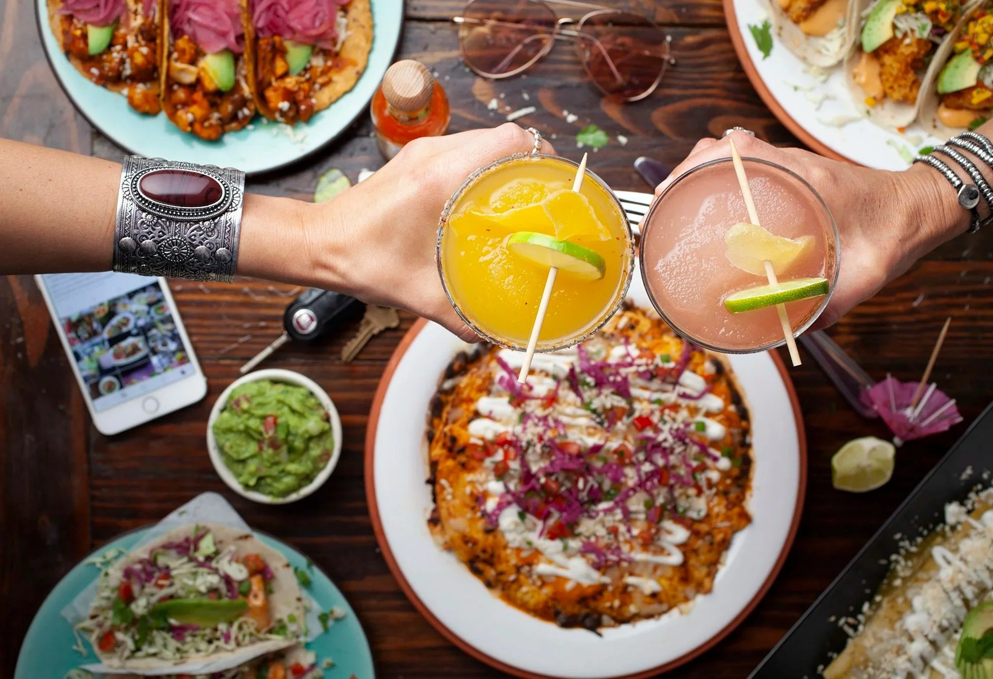 Friends toasting cocktails over a Mexican food spread - backlit beverage photography