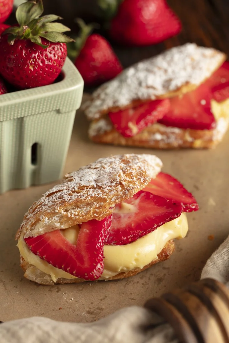 Strawberry cream puff pastry with sliced strawberries and powdered sugar on top, with fresh strawberries in a green container in the background. Los Angeles food photographer and stylist pastry photo shoot