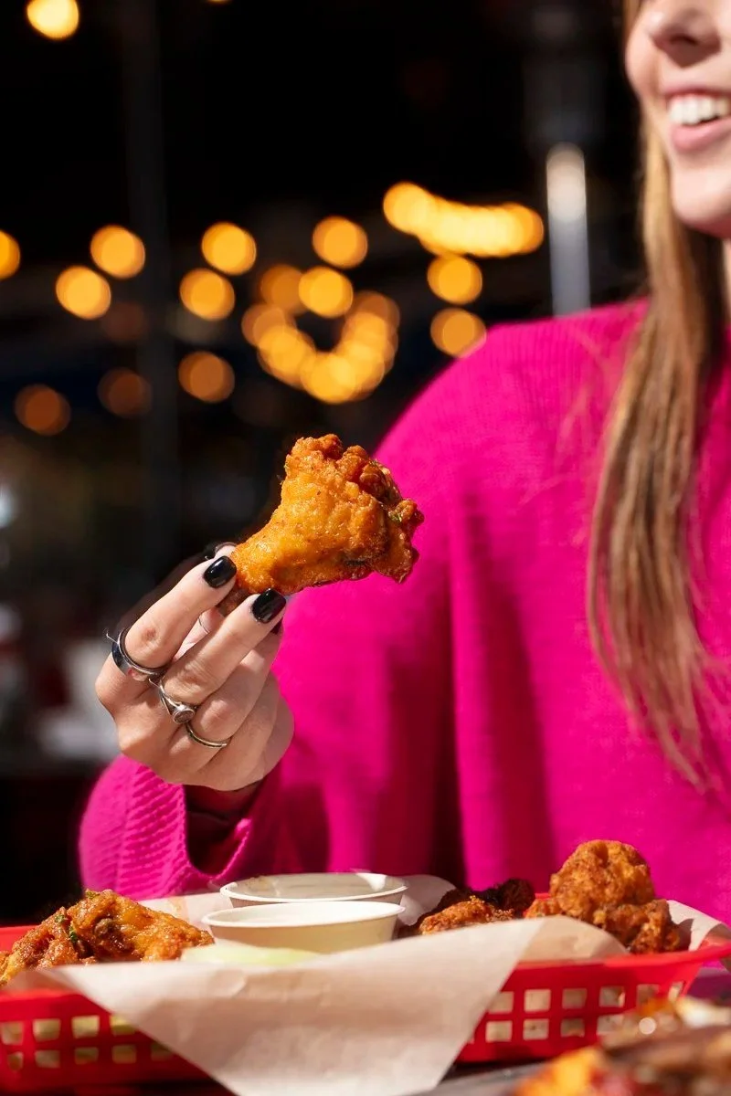 Woman in pink eating chicken wings at a restaurant - restaurant food and lifestyle photography