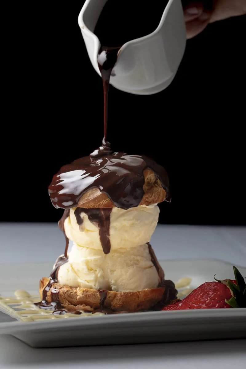Vanilla ice cream served in a waffle bowl topped with chocolate sauce, with a side of strawberries on a white