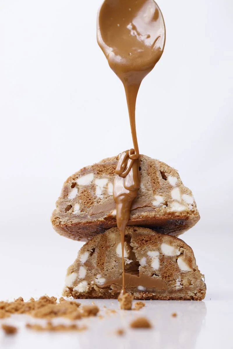 Chocolate chip cookie dough ice cream sandwiches with caramel sauce being poured on top.